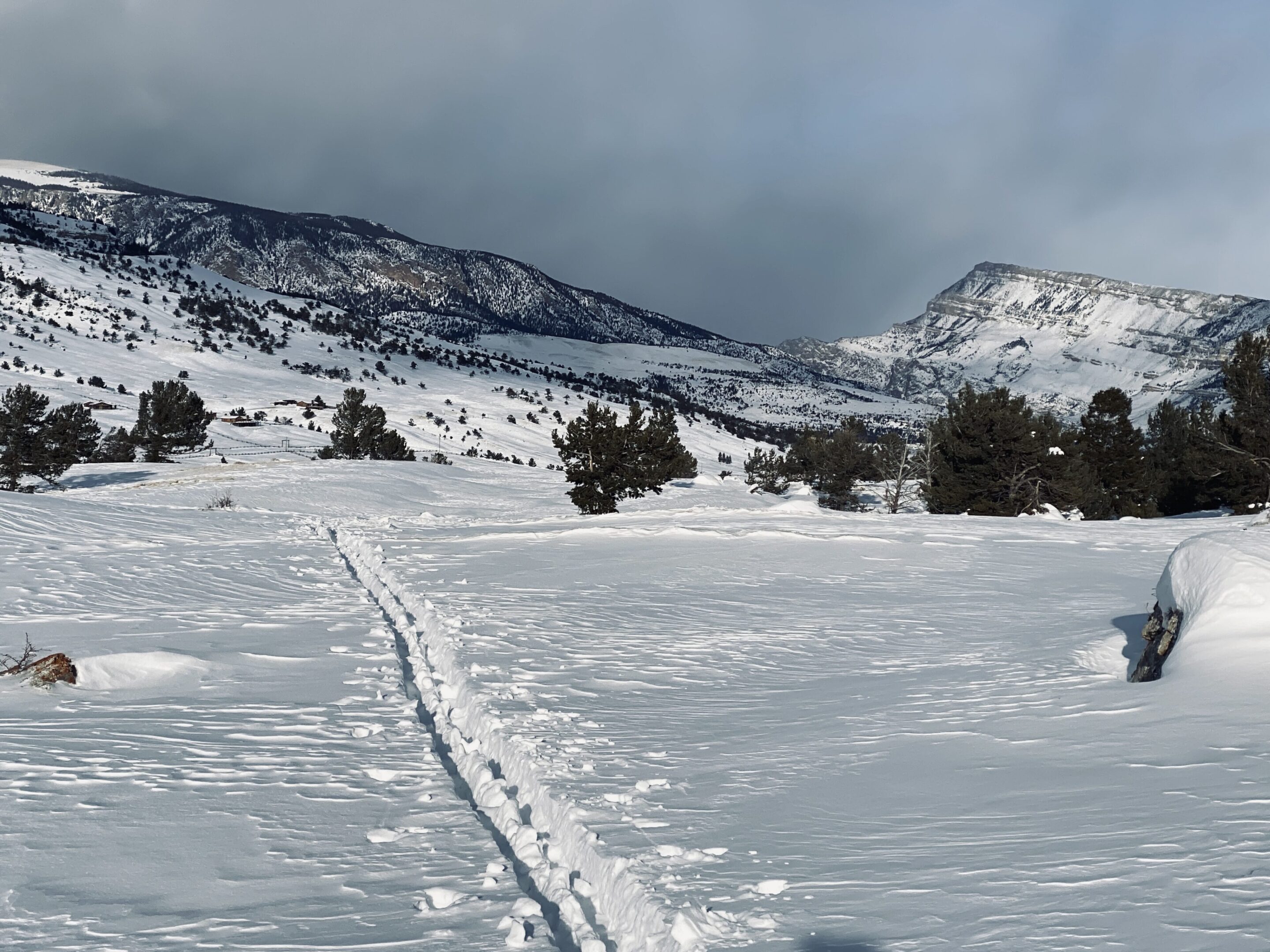 Snow-covered landscape with a trail leading through the snow towards distant mountains.
